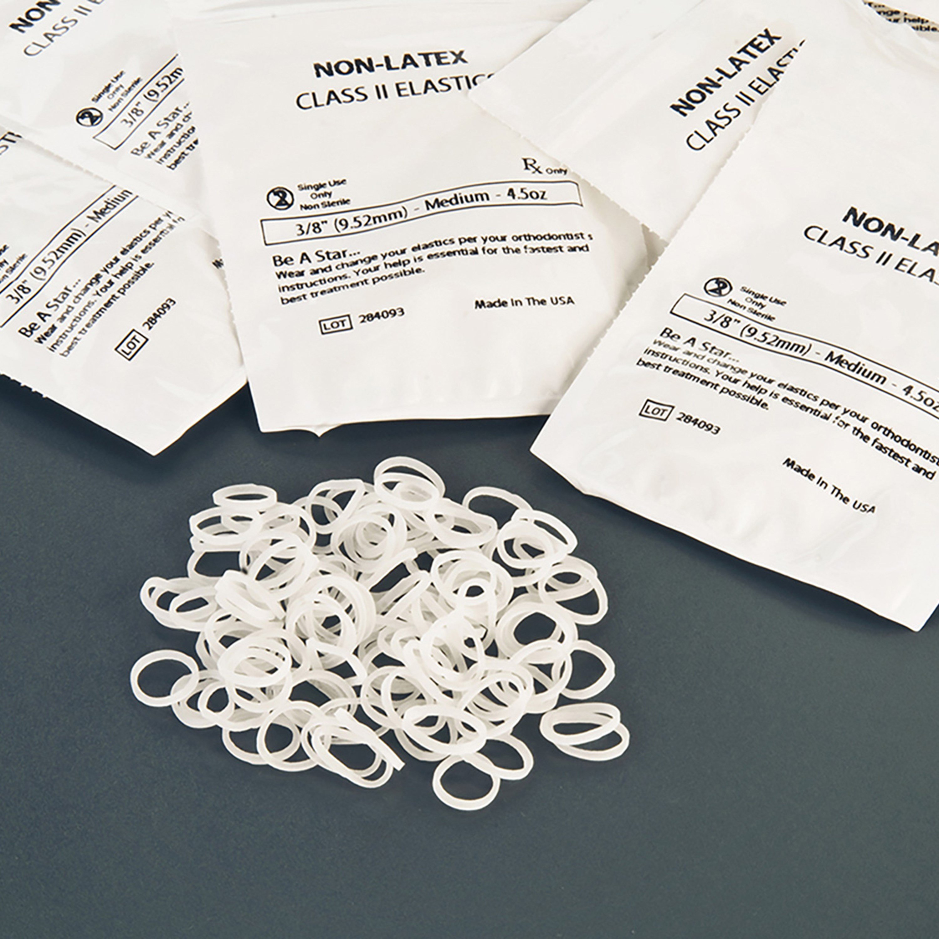 A pile of white non-latex class II elastics in a pile. Their packages are arranged behind them so as to provide product detail. 