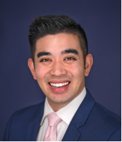 Dr. Brian Baliwas, a man who looks to be in his early thirties in a sharp suit smiles warmly at the camera