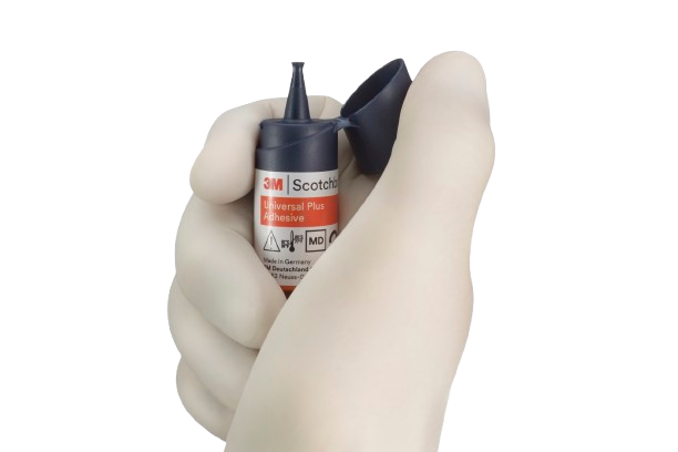 A gloved hand holding the Scotchbond Universal Plus Adhesive on a white background