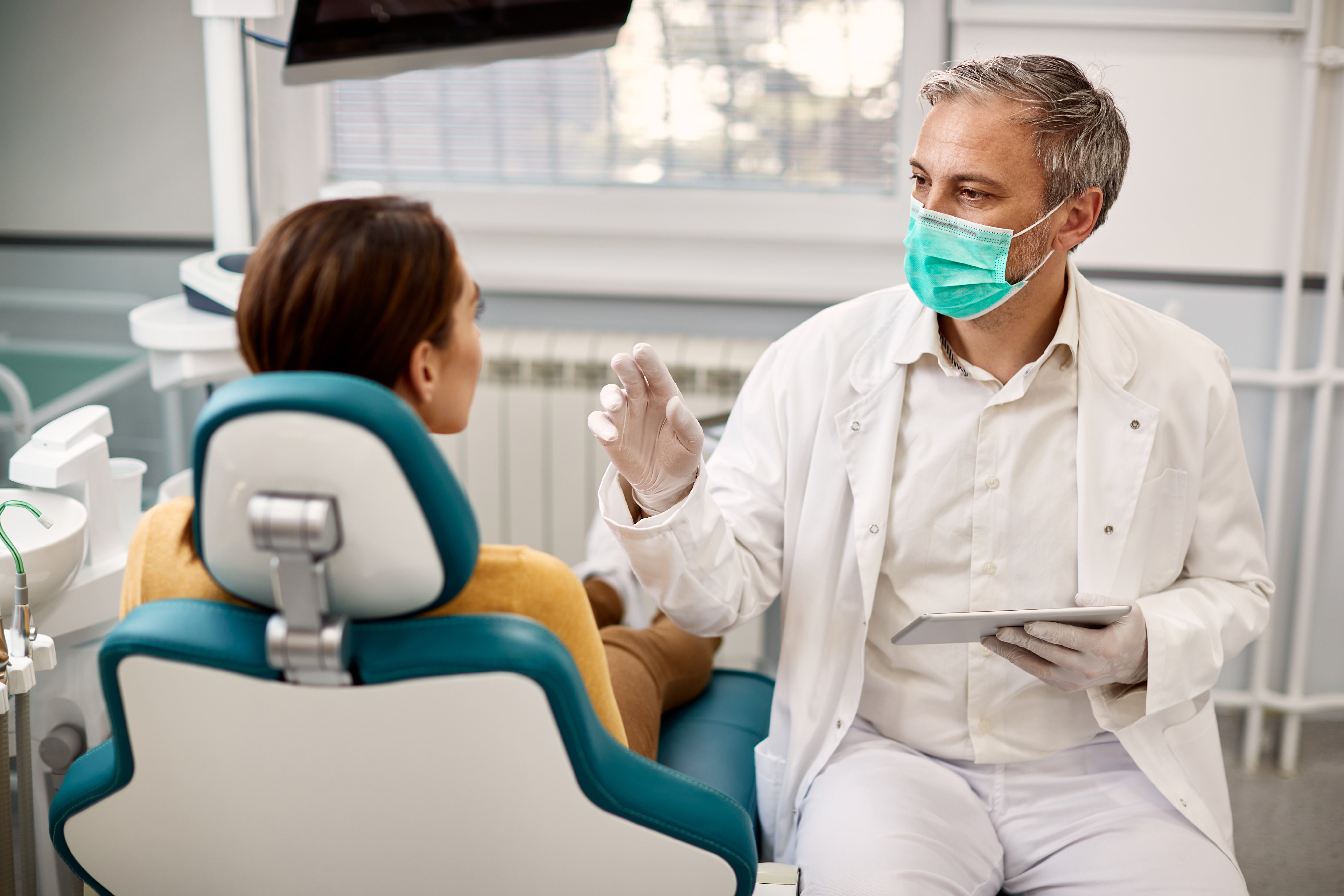 A masked practitioner talks to his patient, in a well-lit practice