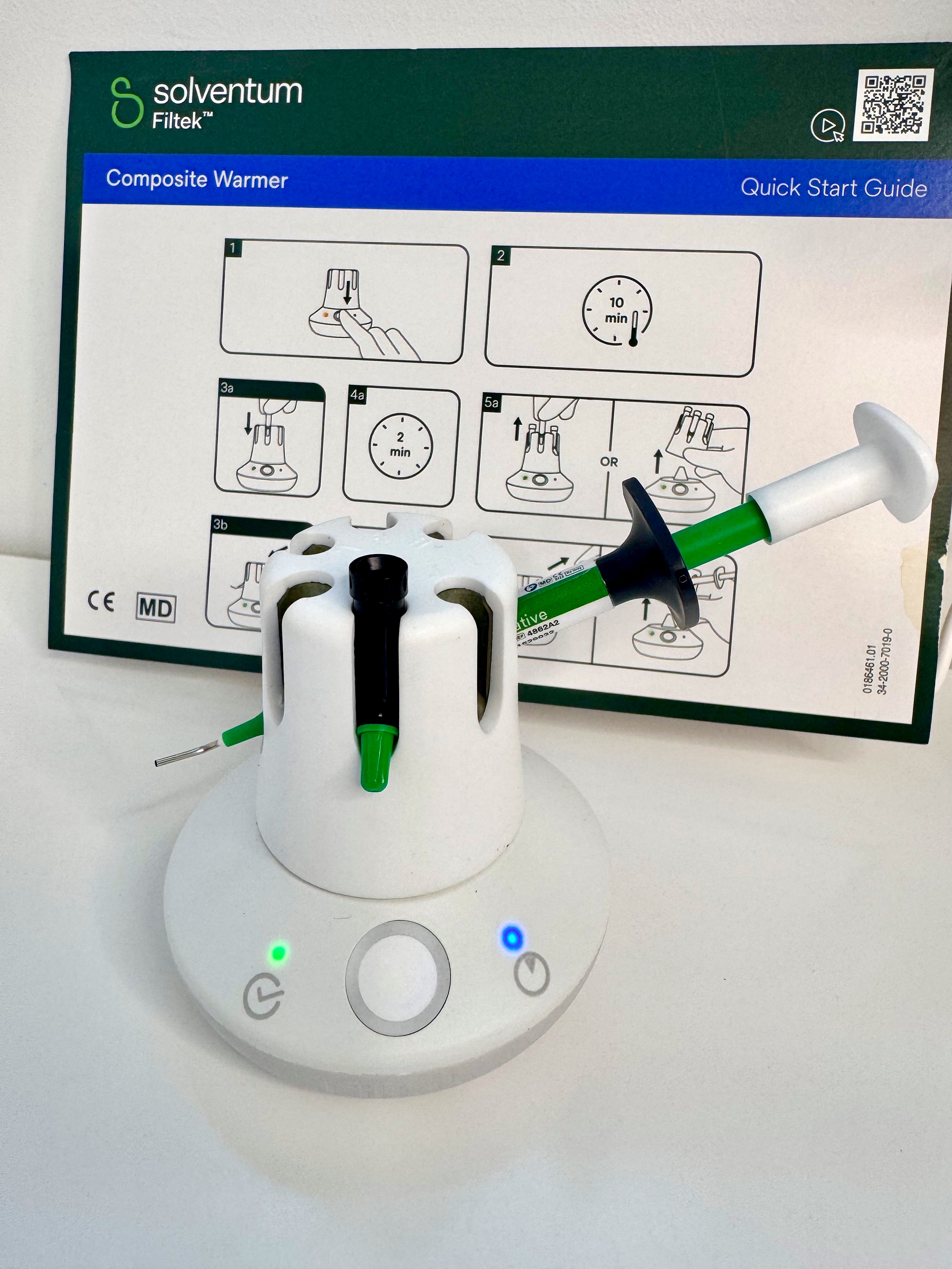 The Filtek Composite warmer with a composite in slot, the warmer sits before a Solventum Infographic